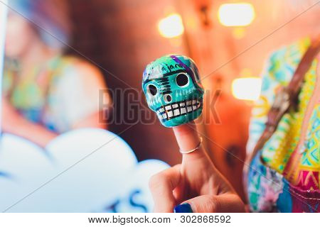 Small Mexican Skulls On A Female Finger On A Colored Background.