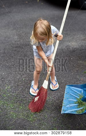 Little Girl Helps Her Parents Collect Grass In The Yard. Seasonal Gardening. Cleaning The Yard
