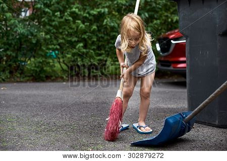 Little Girl Helps Her Parents Collect Grass In The Yard. Seasonal Gardening. Cleaning The Yard
