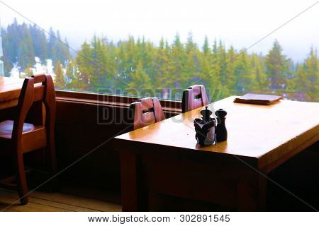 Tables And Chairs At A Restaurant Inside A Lodge Besides A Window With Views Of The Forested Mountai