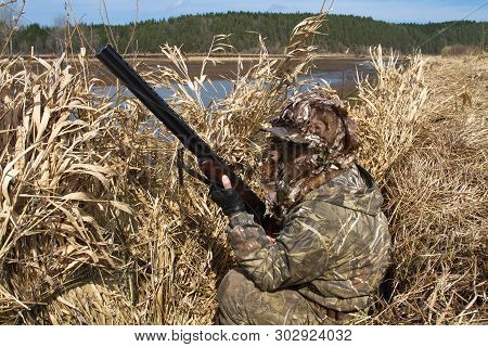 Duck Hunter With A Shotgun Sits In A Hunting Blind Of Reeds On The Lake