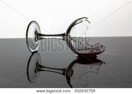 Broken Wine Glass With Red Wine Which Is Laying On The Wet Surface. White Background