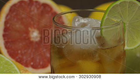 Liquor In A Glass Cup With Ice Cubes. Close-up Shot. Fresh Fruits In The Background. Lime Grapefruit