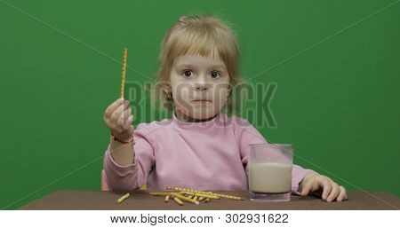 The Child Eats Cookies. A Little Girl Is Eating Cookies And Drink Cacao Sitting On The Table. Green 