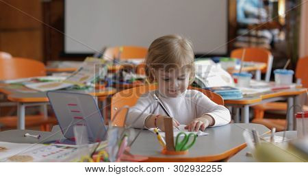 Girl Drawing At The Table In Classroom. Education Process. Happy Three Years Old Child Sitting At A 