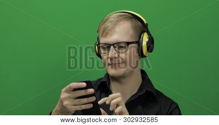 Guy Listens To Music In Wireless Yellow Headphones. Portrait Of Attractive Man Using Smart Phone For