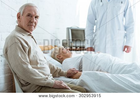 Cropped View Of Doctor, Senior Man And Sick Senior Woman Lying On Bed In Hospital