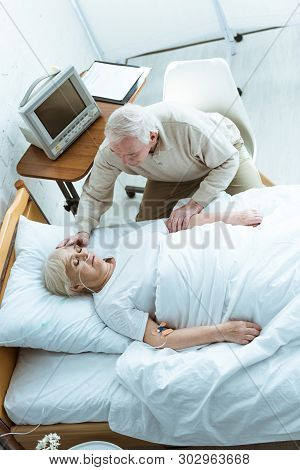 Overhead View Of Senior Man Stroking Wife In Coma In Clinic