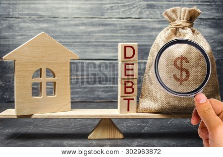 Money Bag And Wooden Blocks With The Word Debt And A Miniature House On The Scales. Payment Of Debt 