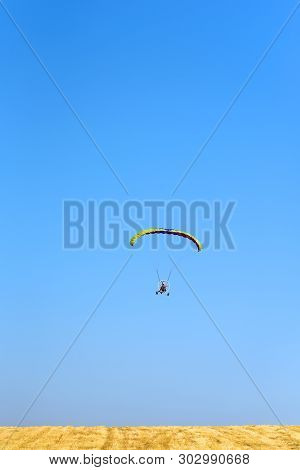 Powered Paraglider Parachute Against Blue Sky And Yellow Field. Paramotor  Flying In Sunny Day. Free