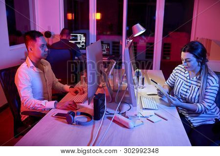 Young Asian Businessman Sitting At The Table And Working On Computer While Young Businesswoman Sitti