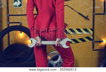 Stylish Mechanic Girl In Trendy Clothes Is Holding A Wrench On The Background Of The Workshop Of An 
