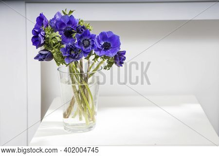 Bouquet Of The Blue Anemones In A Glass Vase On A White Table Near The Pale Gray Wall. Vertical Fram