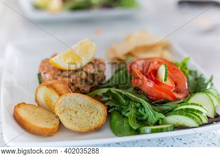 An Aesthetic Shot Of French Dish Tartare De Saumon Avec Fleur De Tomate, Placed On A White Plate, Bl