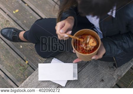White Envelope Mockup. The Girl On The Bench Eats Soup With Seafood Shrimp.