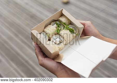 The Girl Opens A Cardboard Bag With A Set Of Sushi. Seafood Delivery Concept.