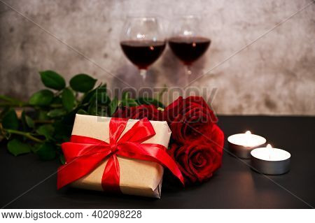 A Gift With Rose,candles And Awo Glasses Of Red Wine On Cement Background. St. Valentine's Theme