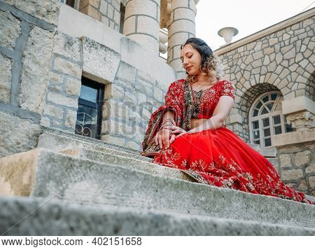 Young Beautiful Indian Woman Walks On Ancient Architecture Streets Of City Of India Dressed In Red S