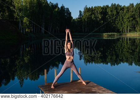 Young Woman Relaxing By The Lake At Sunset, Harms Outstretched. Doing Youga In The Morning At Forest