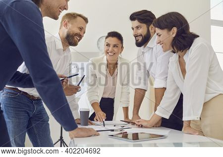 Group Of Young Smiling Business People Discussing New Project Or Startup Idea During Meeting Togethe