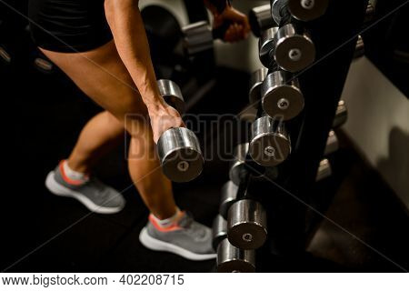 Close-up Of Strong Female Hand With Silver Dumbbell Near Rack With Other Dumbbells
