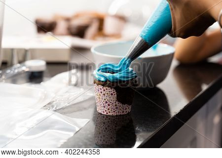 Woman Adding Blue Frosting To Chocalate Cupcake In Messy Kitchen