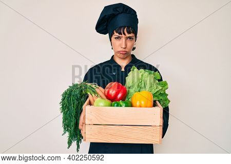 Beautiful brunettte woman chef holding fresh veggetables depressed and worry for distress, crying angry and afraid. sad expression. 