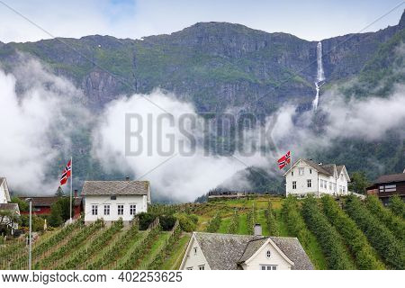 Ullensvang Town In Norway. Misty Mountains And A Waterfall. Norwegian Landscape.