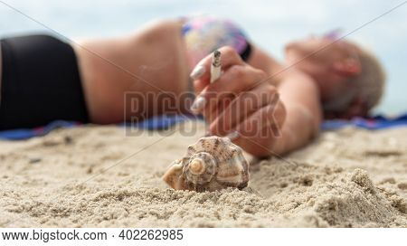 Smoking On The Beach And Shaking Off Cigarette Ash Into Rapan