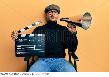 Handsome man with tattoos holding video film clapboard and louder relaxed with serious expression on face. simple and natural looking at the camera. 