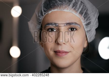 Close-up Of The Woman Face In Cap With White Anesthetic Cream On The Eyebrows Before The Permanent M