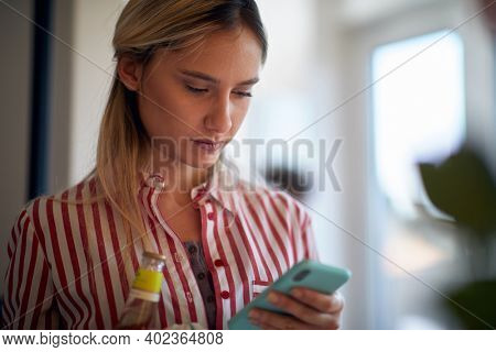 A young girl in a relaxed atmopshere at home enjoying a drink and texting on smartphone. Home, leisure