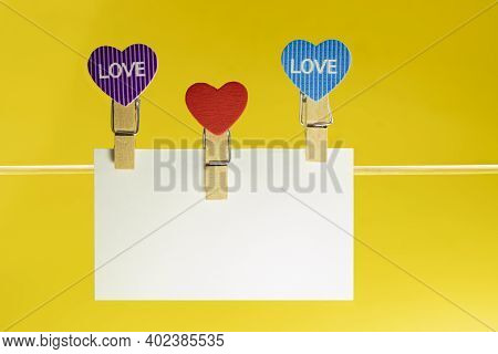 White Paper Plaque With Space For Text With Heart-shaped Clothespins On A Cord. Bright Yellow Backgr