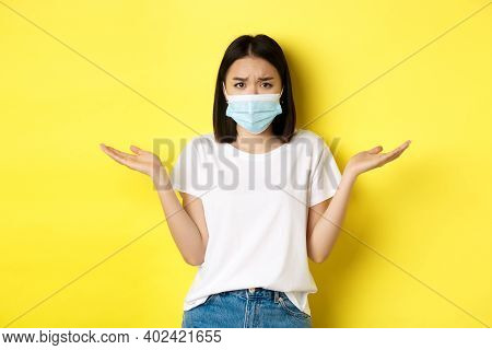 Covid-19, Quarantine And Social Distancing Concept. Confused Asian Woman In Medical Mask Shrugging S