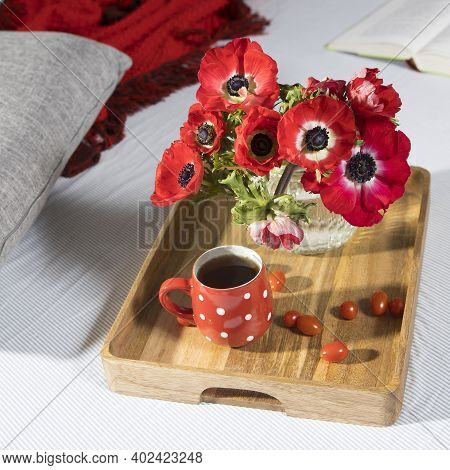 A Bouquet Of Red Anemones In A Glass Vase On A Wooden Tray On The Bed. White Polka Dot Cup With Tea.