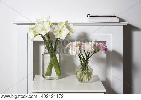 A Bouquet Of Pink Persian Buttercups In A Glass Vase And Two Wrapped Gifts On A White Table In Front