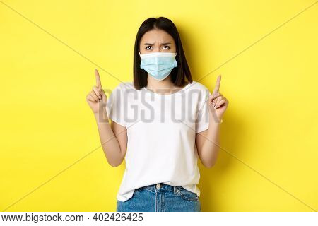 Covid-19, Pandemic And Social Distancing Concept. Disappointed Asian Girl In Medical Mask, Frowning 