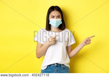Covid-19, Pandemic And Social Distancing Concept. Disappointed Asian Girl In Medical Mask, Frowning 