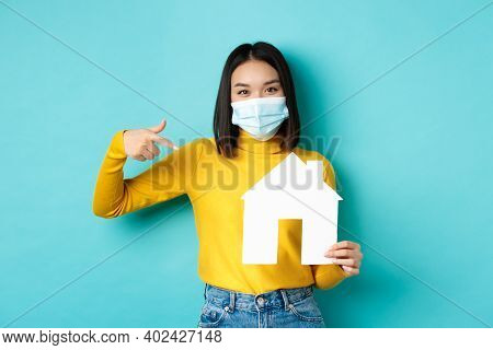 Covid-19, Pandemic And Real Estate Concept. Cheerful Asian Woman Smiling In Medical Mask, Showing Pa