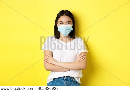 Covid, Health Care And Pandemic Concept. Asian Woman In White T-shirt And Medical Mask Cross Arms On