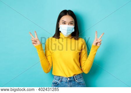 Covid-19, Social Distancing And Pandemic Concept. Kawaii Asian Woman Showing Peace Signs And Smiling