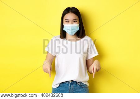 Covid-19, Pandemic And Social Distancing Concept. Happy Asian Woman In Medical Mask, Showing Adverti