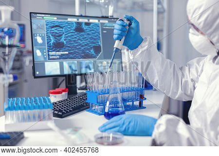 Medic Assistant Working In Biochemistry Lab Working With Automatic Pipette Wearing Protection Suit. 