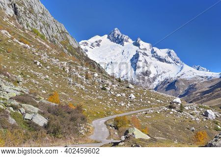 Road Crossing Mountain With Snowy Peak  Background Under Blue Sky In Euroean Alps