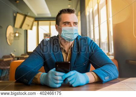 Young European Guy Businessman In Protective Gloves And A Medical Mask Spends Time On The Phone And 