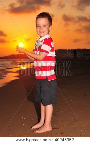 Little boy holding sun on sunset.