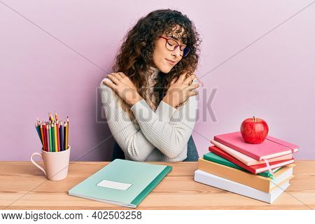 Young hispanic girl studying for school exam hugging oneself happy and positive, smiling confident. self love and self care 