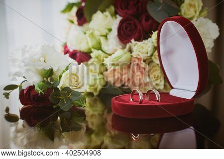 Close Up View Of Wedding Rings In A Red Velvet Box And  Flowers On A Glass Table In The Hotel Room.