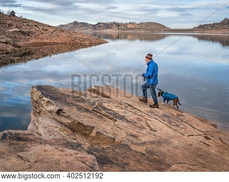 senior male hiker is waling with pitbull dog on a shore of mountain lake at foothills of Rocky Mountains, Horsetooth Reservoir - a popular recreational area in northern Colorado in fall or winter 