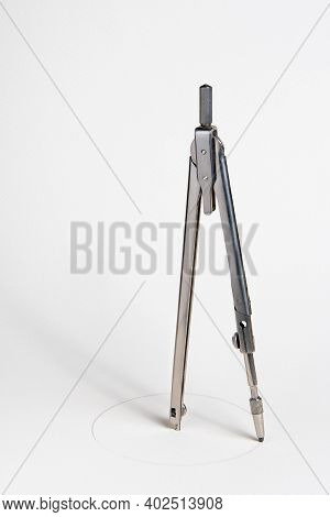 A Vintage Compass Stands With Its Foot In The Center And Draws A Circle On A White Sheet Of Paper